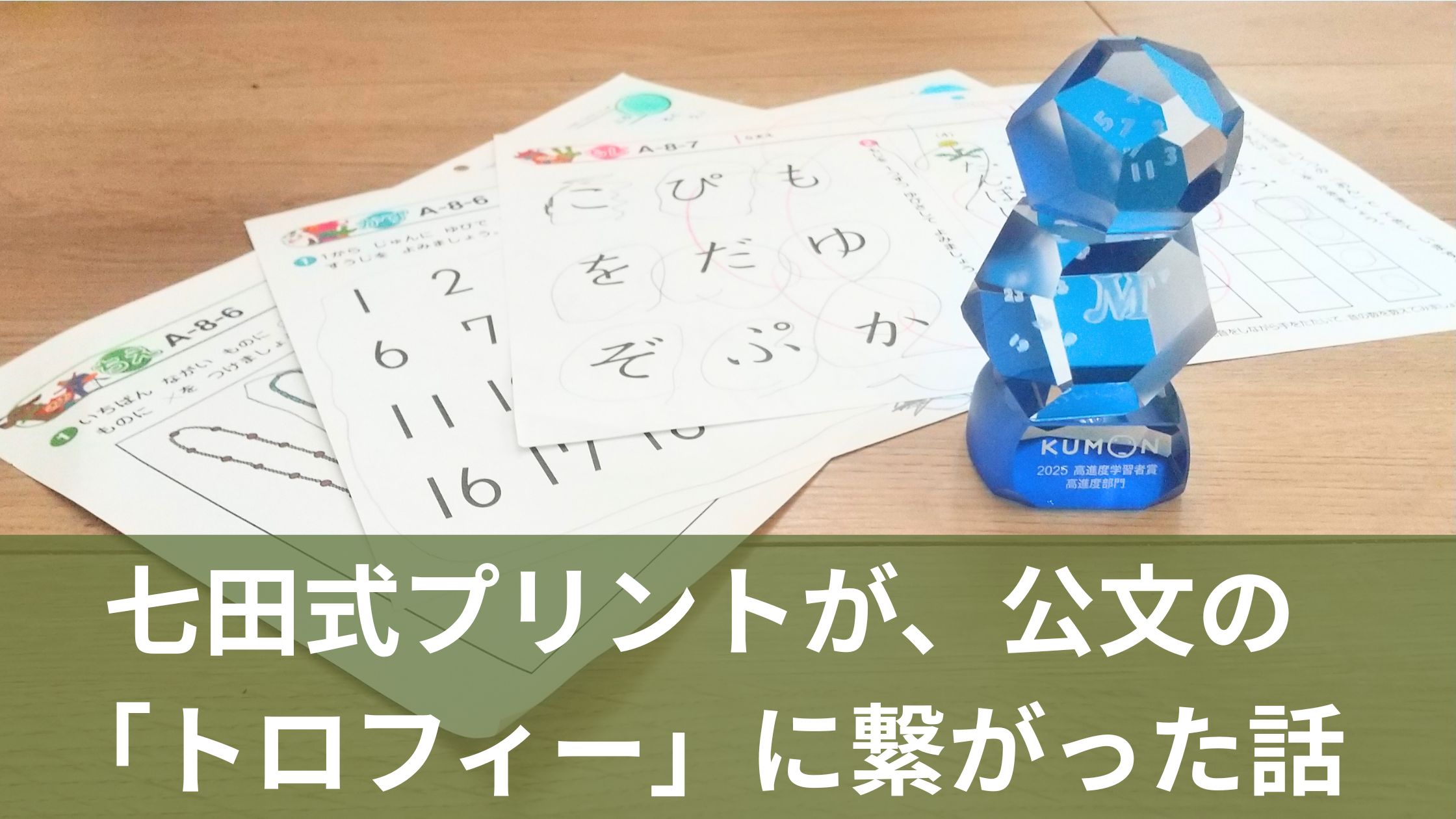 七田式プリントのAプリント(たどたどしい文字の書き込み)と、公文式の青い高進度学習者トロフィーが並んで置かれている様子
